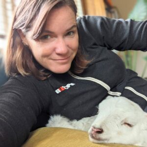 Girl in zip up hoodie smiles while sitting with a lamb